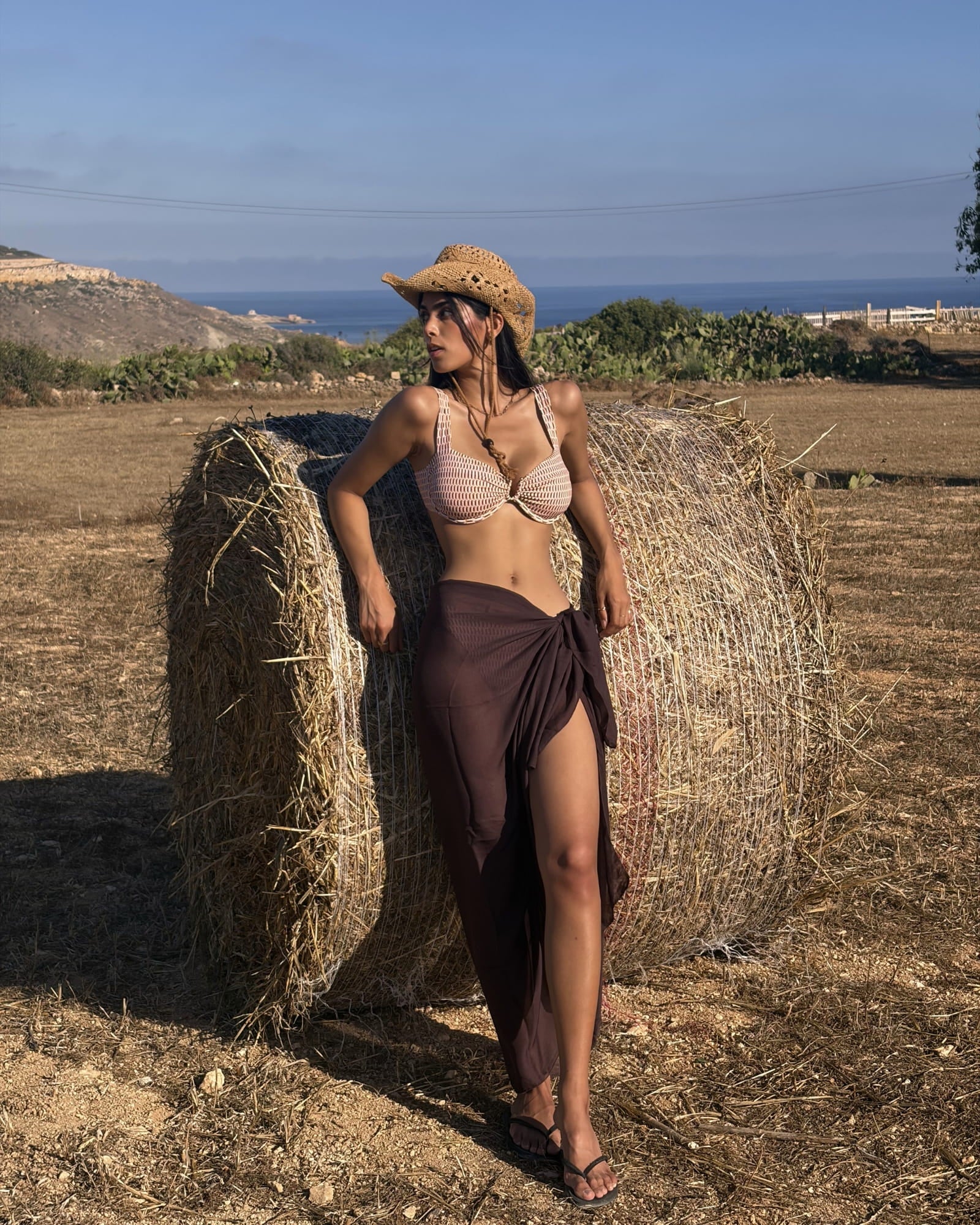 Full-length Toco Swim Chocolate brown maxi sarong tied at the waist with a thigh slit, worn with a straw hat
